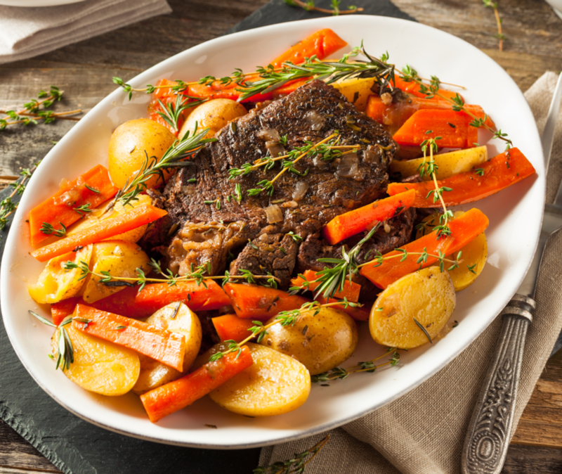 white platter of pot roast surrounded by potatoes and carrots and garnished with thyme