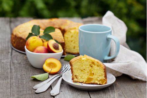 Bowl of peaches, bundt cake, slice of cake, cup of coffee on outdoor wooden table