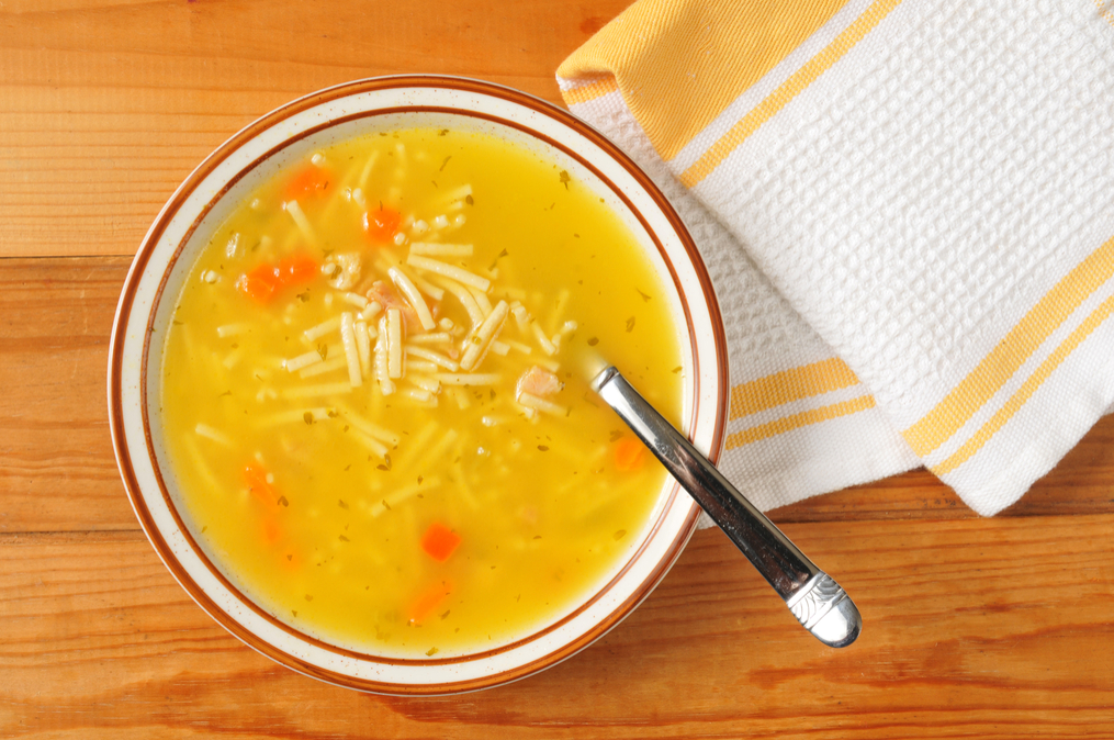 bowl of chicken soup on rustic background, with spoon