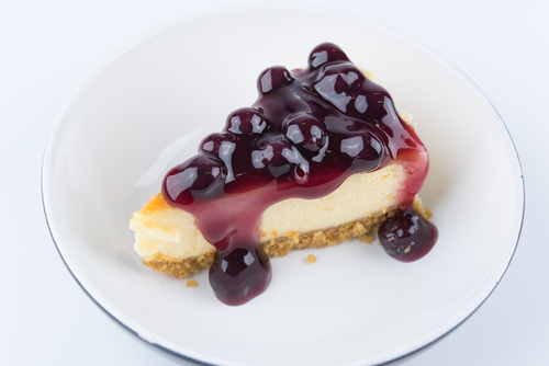 Slice of blueberry cheesecake on white plate on white background