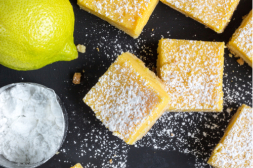 lemon squares and lemon on black background with bowl of powdered sugar