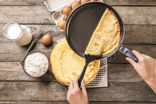 Woman's hand removing crepe from pan with background of crepe ingredients