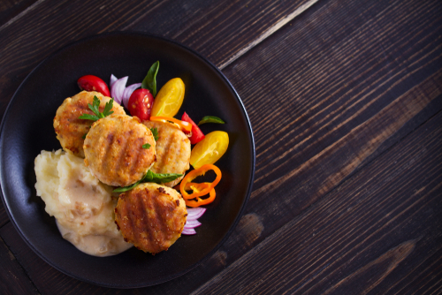 tuna patties on bed of mashed potatoes with colorful vegetables on the side