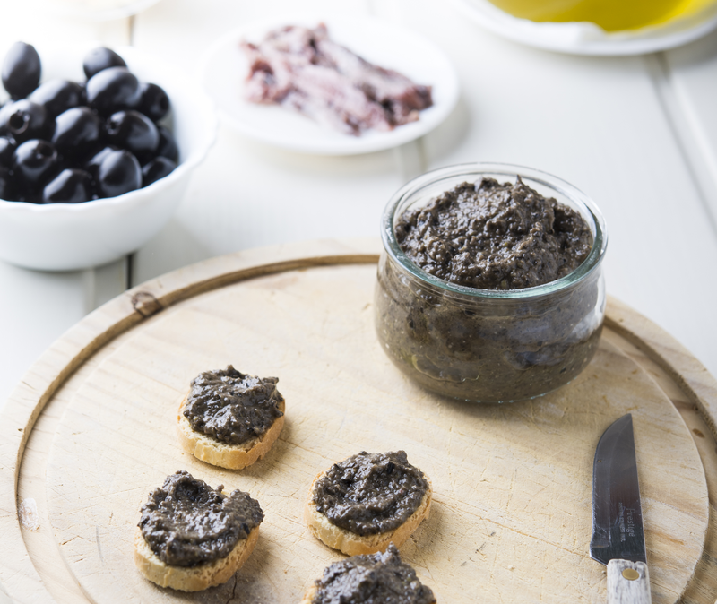 olivada or tapenade on cheese board with small toasts and spreading knife